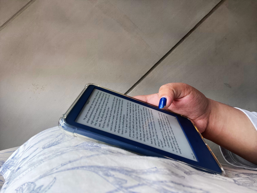 A reader’s hand flipping through the pages of a Kindle e-reader.